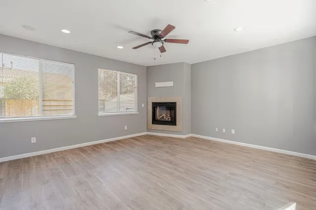 an empty room with wooden floor ceiling fan and windows