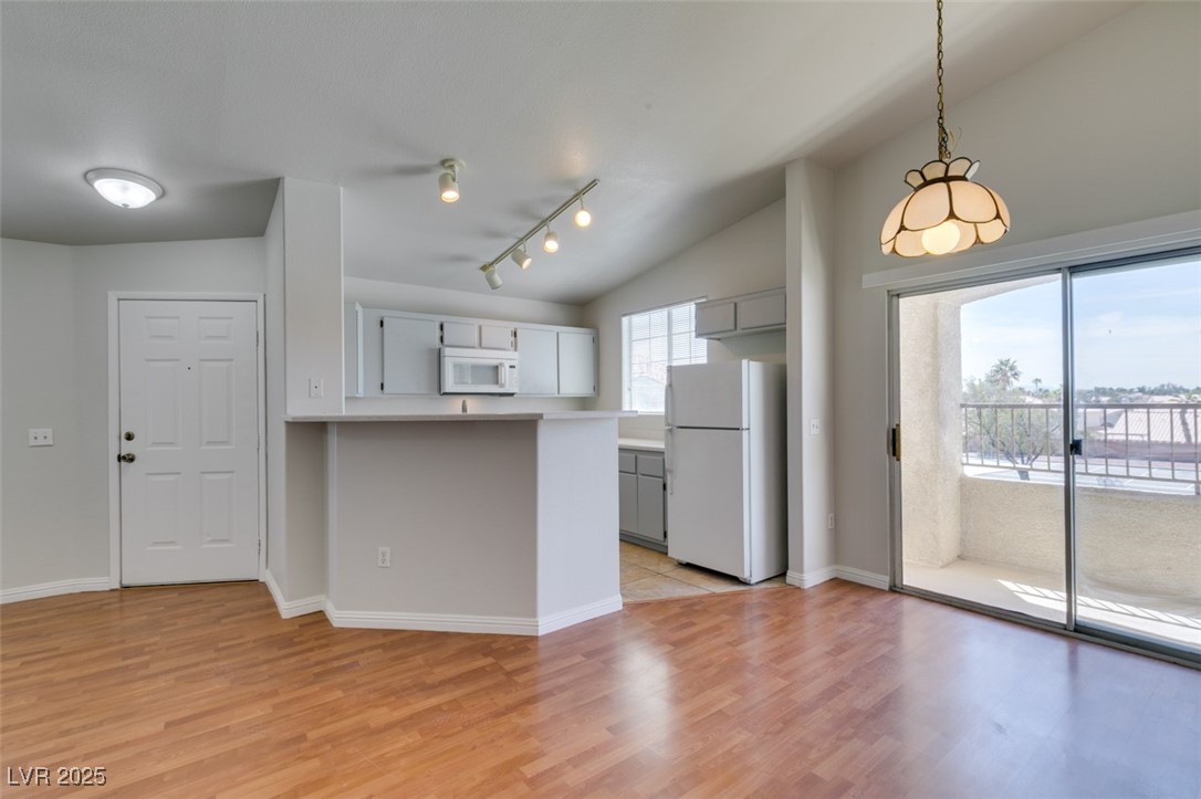 Kitchen featuring white appliances, light wood-style floors, plenty of natural light, rail lighting, and lofted ceiling