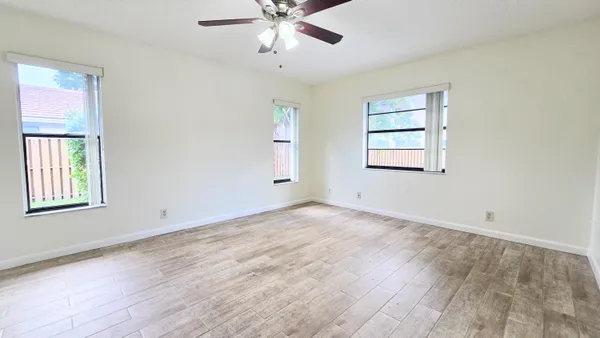 an empty room with wooden floor ceiling fan and windows