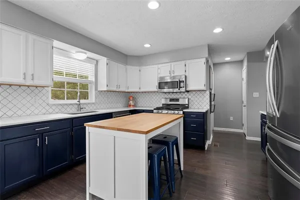 a kitchen with stainless steel appliances granite countertop a refrigerator a sink dishwasher a stove and white cabinets with wooden floor