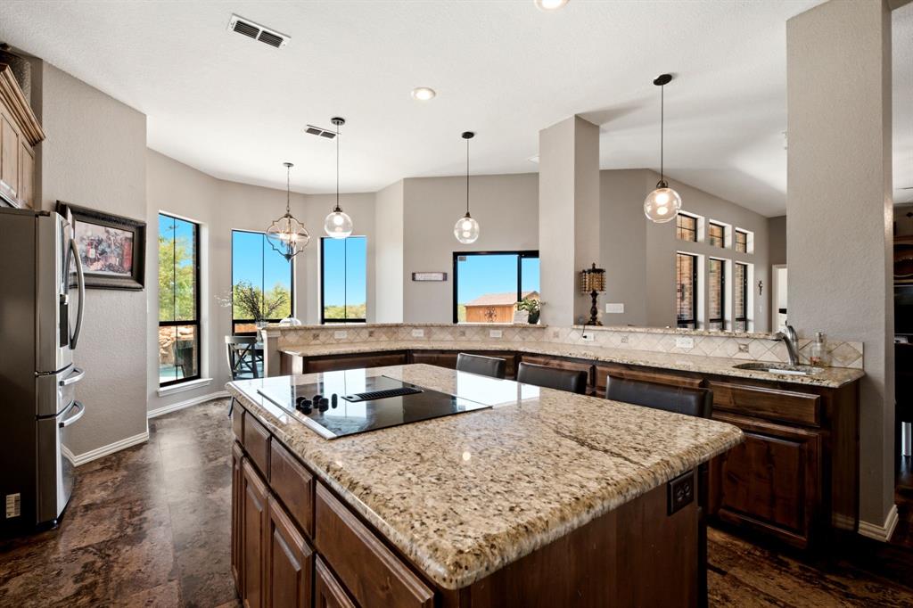 600 Aspen Street Pilot Point, TX 76258 - Photo 18 of 39 Kitchen featuring a large central island with an integrated cooktop and seating, granite countertops, and rich wood cabinetry