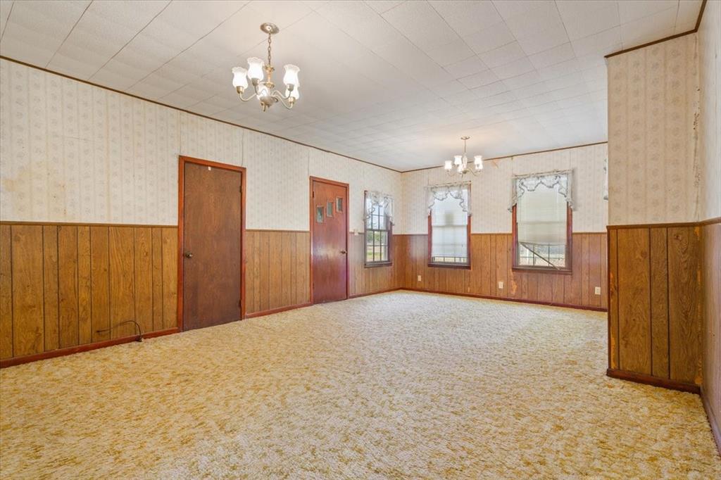 100 County Road 120 C Riesel, TX 76682 - Photo 6 of 25 Empty room featuring a chandelier, wallpapered walls, a wainscoted wall, carpet flooring, and wooden walls