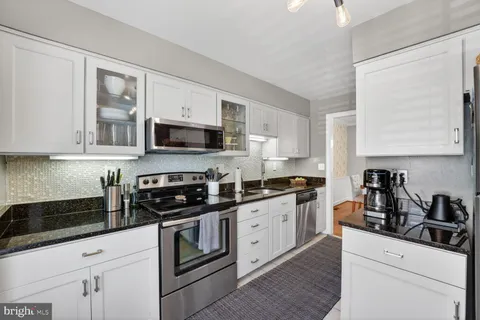 a kitchen with granite countertop white cabinets stainless steel appliances and a counter space