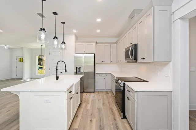 a kitchen with stainless steel appliances a sink a stove a refrigerator and white cabinets