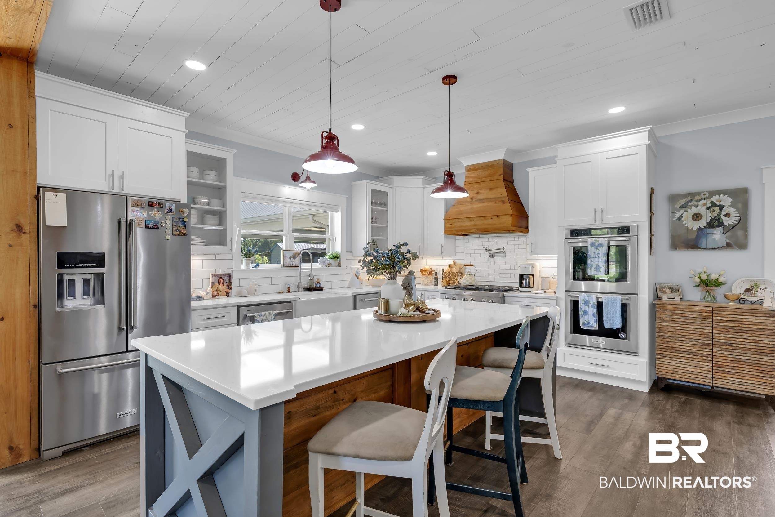 6576 Ranch Loop Road East Grand Bay, AL 36541 - Photo 13 of 39 Kitchen featuring a spacious island with a white countertop and seating, stainless steel appliances, white cabinetry, a wood-finish range hood, and plank wood-finish flooring