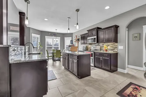 a kitchen with stainless steel appliances kitchen island granite countertop a stove top oven a sink dishwasher a dining table and chairs