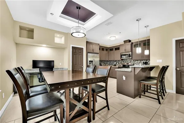 a kitchen with stainless steel appliances kitchen island granite countertop a dining table chairs and a refrigerator