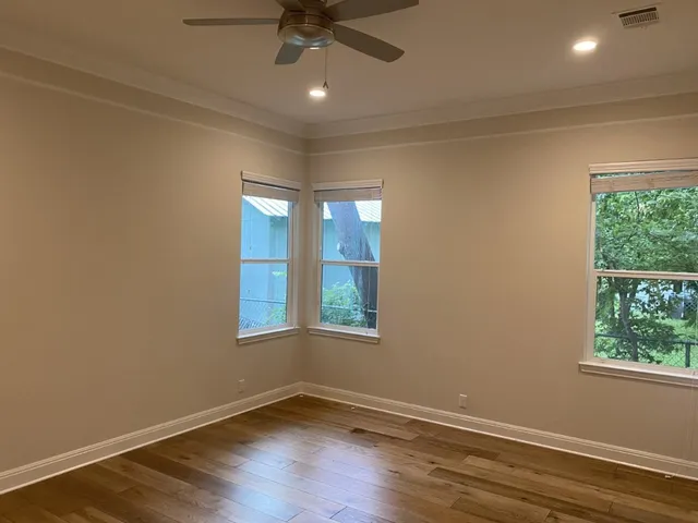 an empty room with wooden floor fan and windows