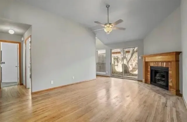an empty room with wooden floor fireplace cabinet and windows