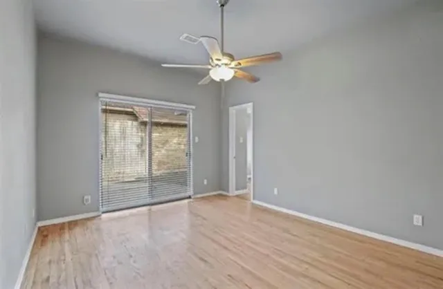 an empty room with wooden floor fan and windows