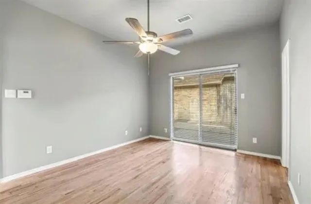 an empty room with wooden floor fan and windows