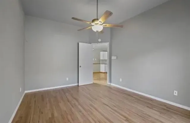 a view of an empty room with wooden floor and a ceiling fan