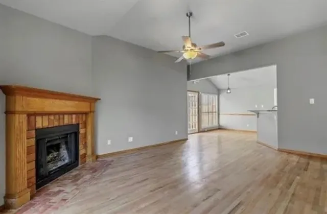 an empty room with wooden floor a fireplace a ceiling fan and a kitchen