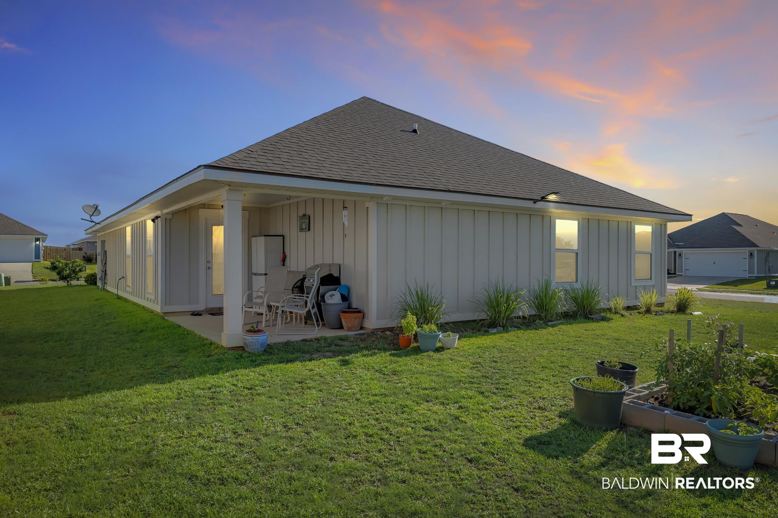 1228 Caper Avenue Foley, AL 36535 - Photo 31 of 54 Rear exterior featuring a covered patio, board and batten siding, multiple windows, and a landscaped yard with garden beds