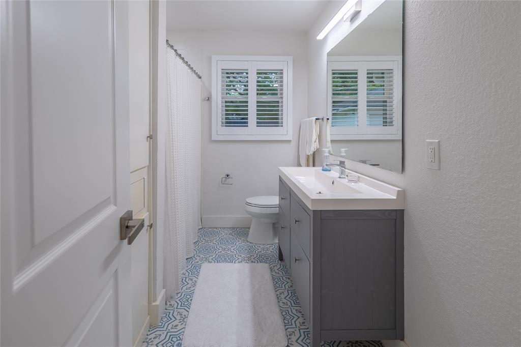 864 Peavy Road Dallas, TX 75218 - Photo 13 of 21 Bathroom featuring patterned floor tiles, a dual-sink vanity with gray cabinetry, and a window with white louvered shutters