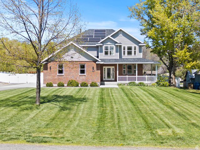 View of front of house with a porch, roof mounted solar panels, brick siding, and a shingled roof