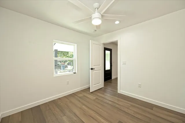an empty room with wooden floor ceiling fan and windows