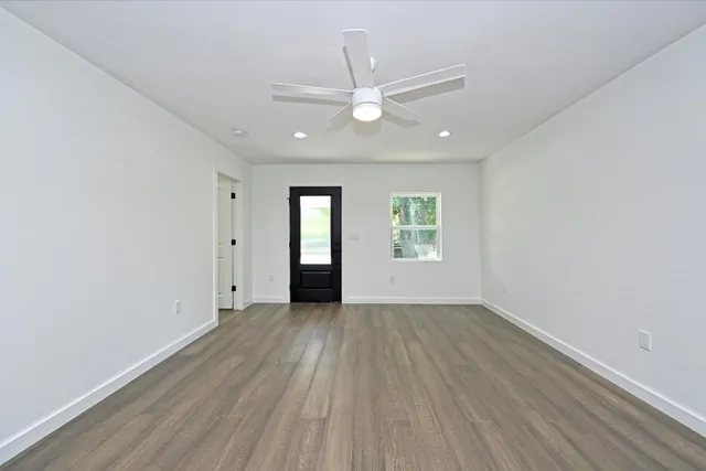 an empty room with wooden floor chandelier fan and windows