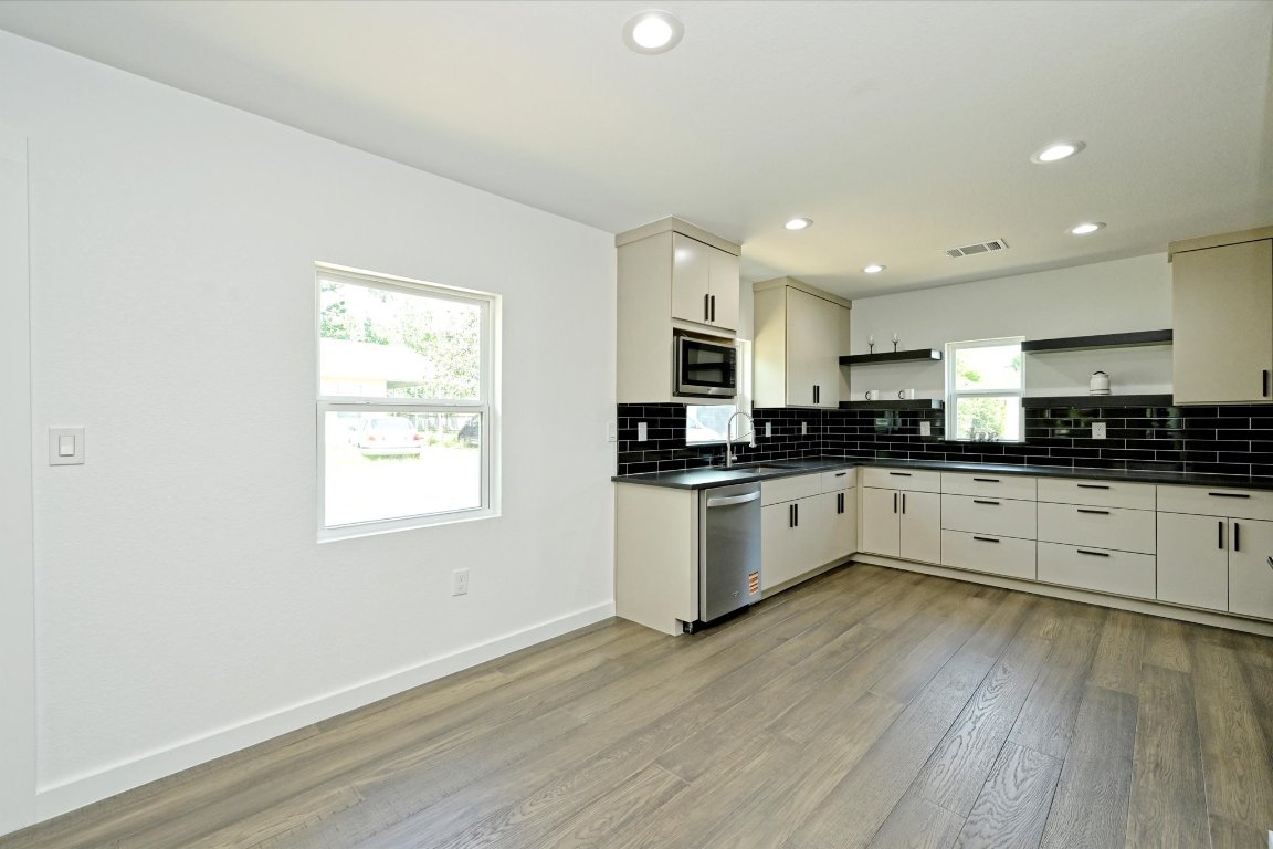710 East 2nd Street Elgin, TX 78621 - Photo 9 of 30 a large white kitchen with granite countertop a stove top oven a sink dishwasher and white cabinets with wooden floor