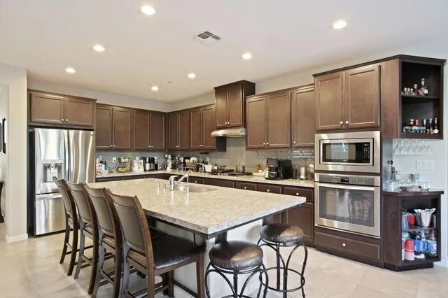 a kitchen with stainless steel appliances granite countertop a stove a refrigerator a microwave oven a sink with island and chairs