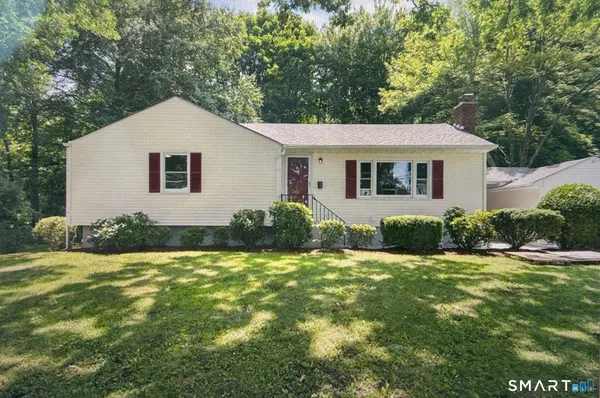 a house that is sitting in the grass with large trees and plants