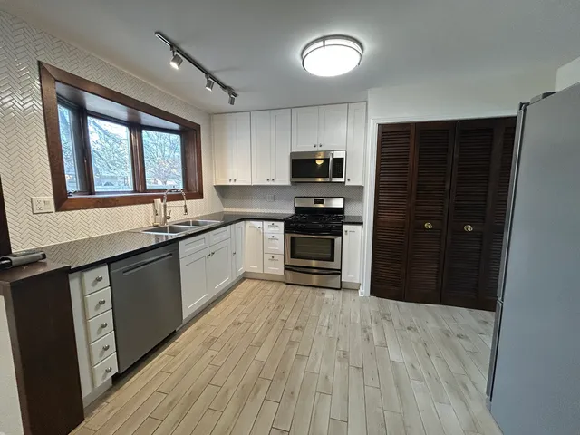 a kitchen with stainless steel appliances granite countertop a refrigerator a sink dishwasher a stove and white countertops with wooden floor