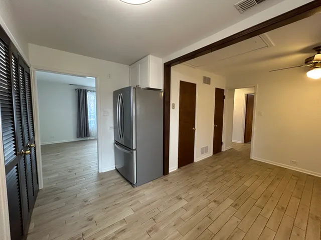 a view of a refrigerator in kitchen and an empty room with wooden floor