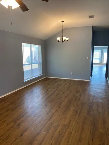 an empty room with wooden floor chandelier fan and windows