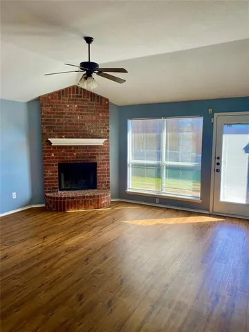 a view of an empty room with wooden floor fireplace and a window