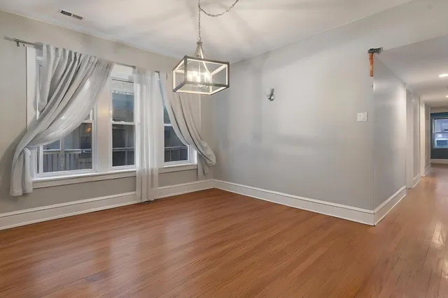 a view of empty room with wooden floor chandelier and windows