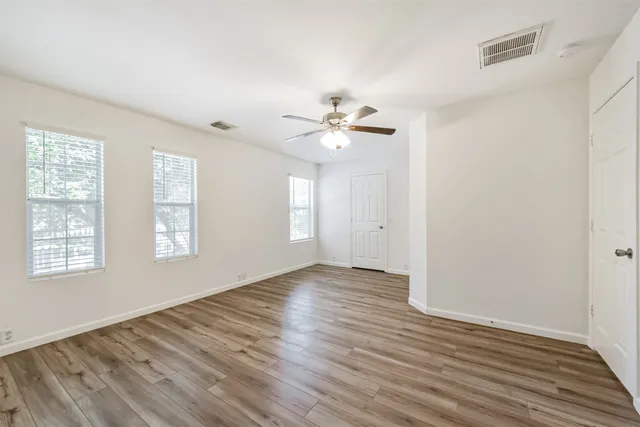 an empty room with wooden floor ceiling fan and windows