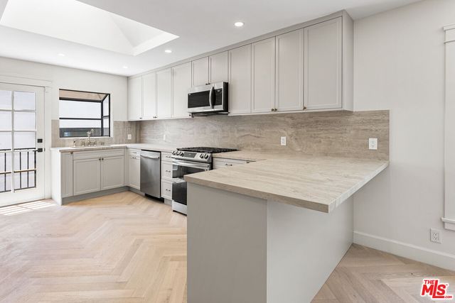 a kitchen with stainless steel appliances granite countertop a stove top oven a sink dishwasher and a refrigerator with wooden floor