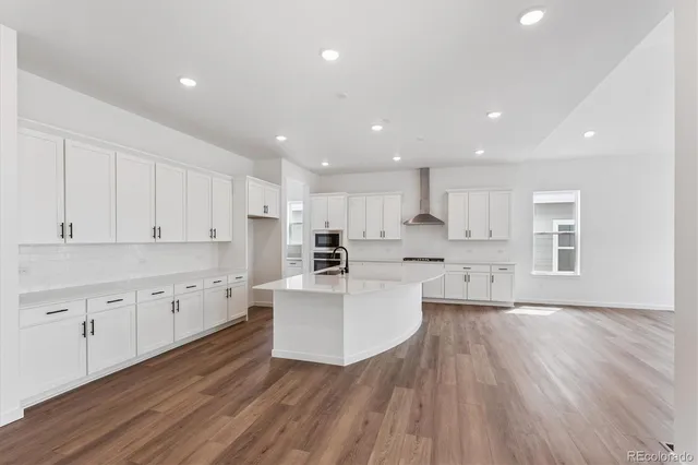 a large white kitchen with wooden floors and white stainless steel appliances