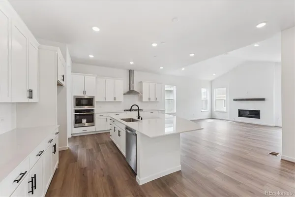 a large kitchen with stainless steel appliances granite countertop a large center island a stove a refrigerator white cabinets and wooden floor