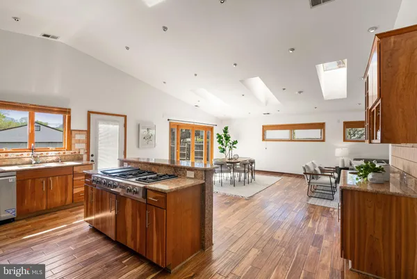 a large kitchen with stainless steel appliances granite countertop a stove top oven a sink dishwasher a dining table and chairs with wooden floor