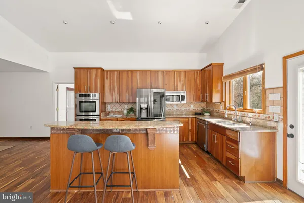 a kitchen with stainless steel appliances kitchen island granite countertop a stove top oven a sink dishwasher a dining table and chairs with wooden floor
