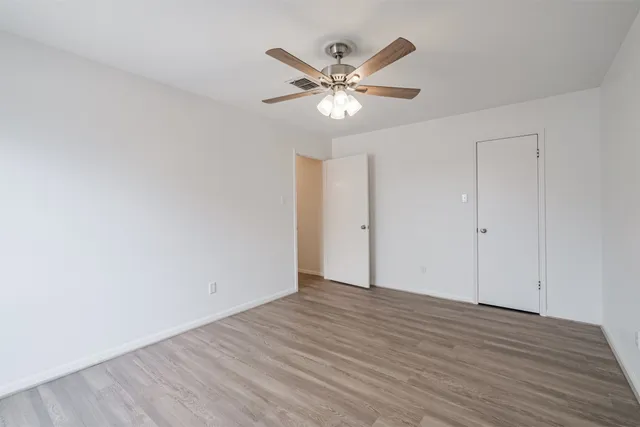 a view of an empty room with wooden floor and a ceiling fan