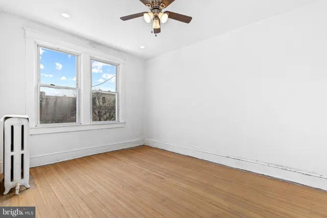 an empty room with wooden floor fan and windows