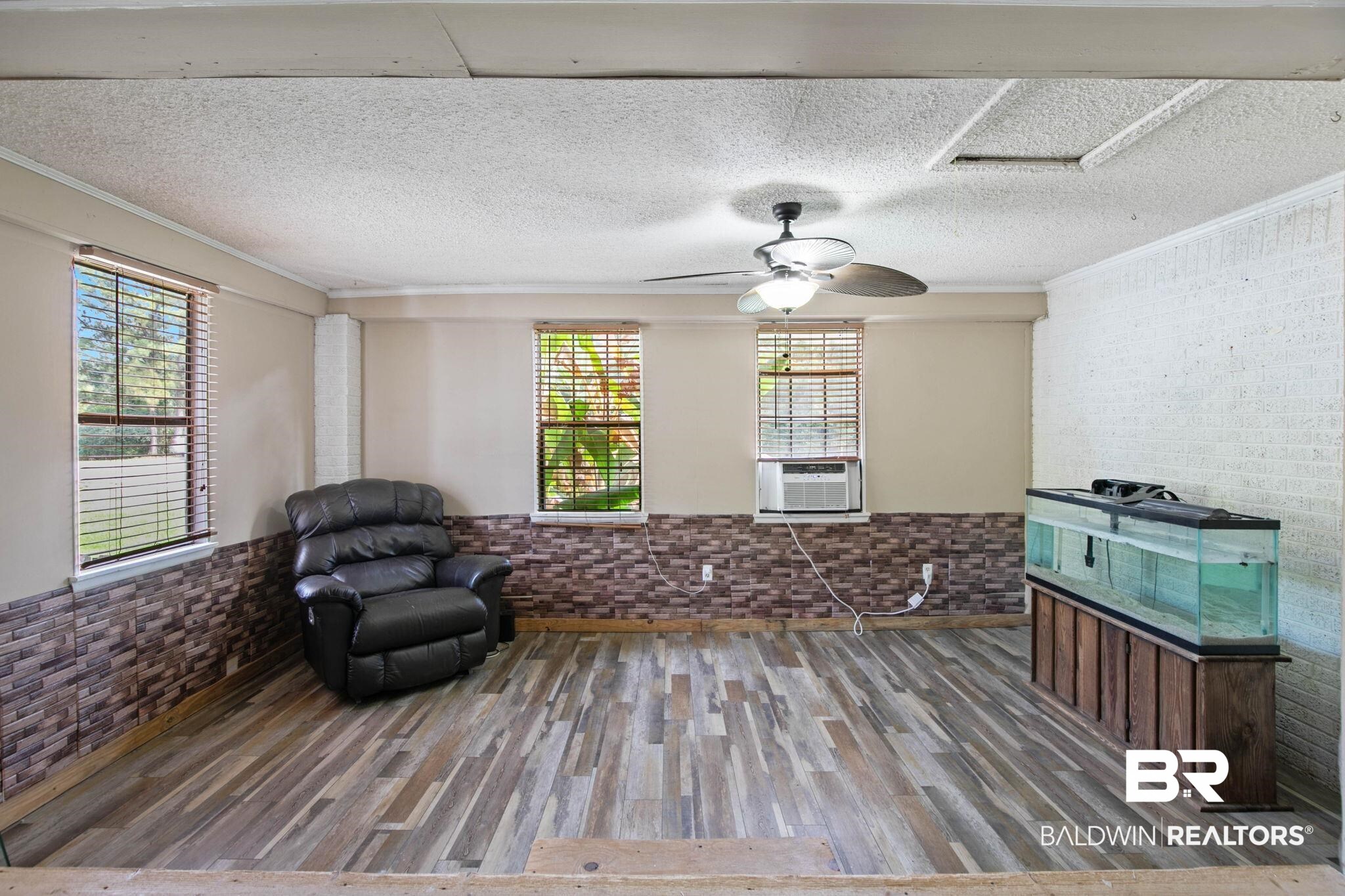 23240 County Road 47 Perdido, AL 36562 - Photo 7 of 29 Unfurnished room with wood finished floors, a wainscoted wall, a textured ceiling, crown molding, and brick wall