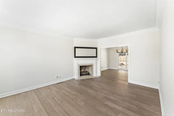 a view of an empty room with wooden floor fireplace and a window