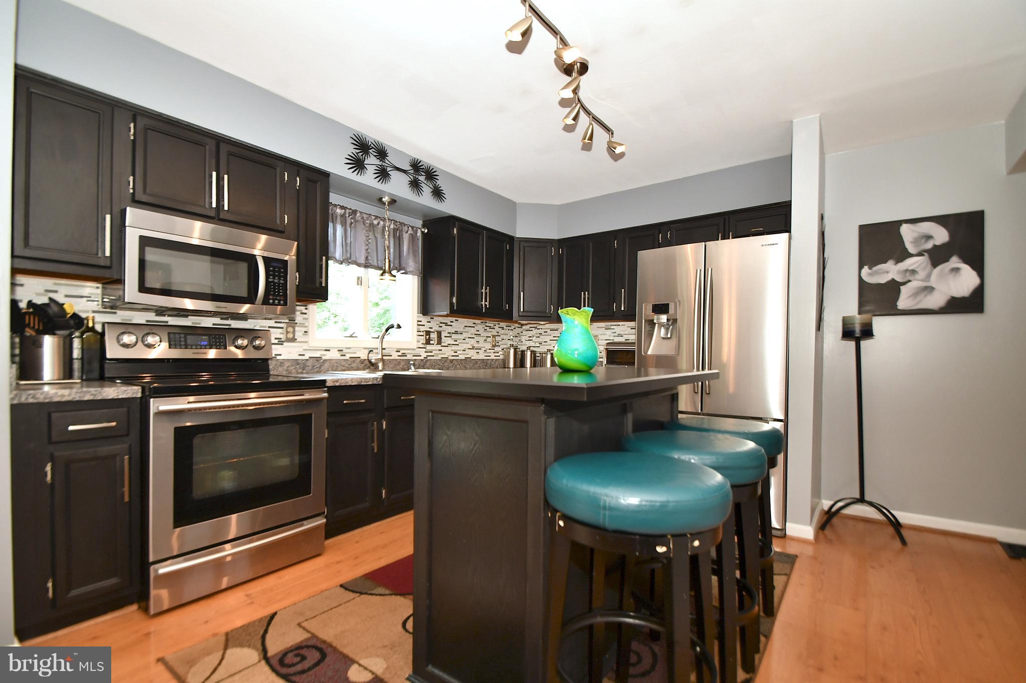 8126 Old Philadelphia Road Baltimore, MD 21237 - Photo 8 of 30 a kitchen with stainless steel appliances a stove refrigerator a sink dishwasher a dining table and chairs with wooden floor