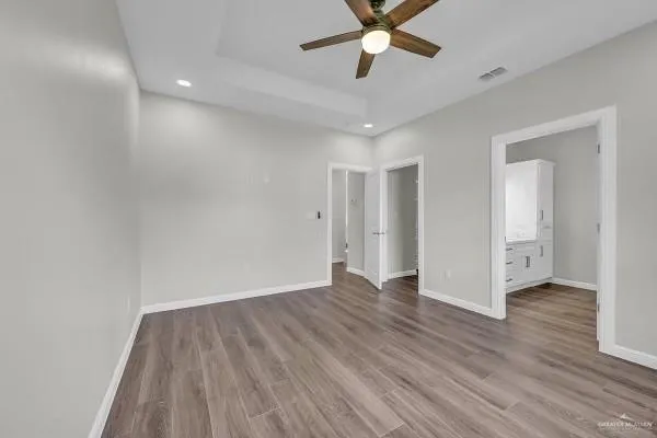 a view of an empty room with wooden floor and a ceiling fan