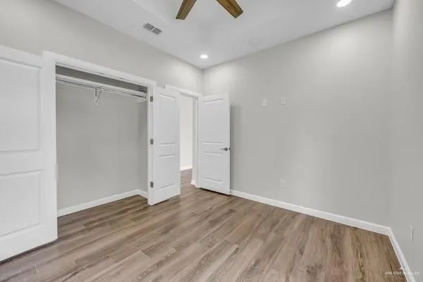 a view of an empty room with wooden floor and a ceiling fan