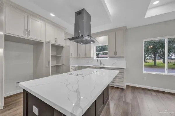 a very nice looking kitchen with granite countertop a stove a sink a refrigerator and white cabinets with wooden floor