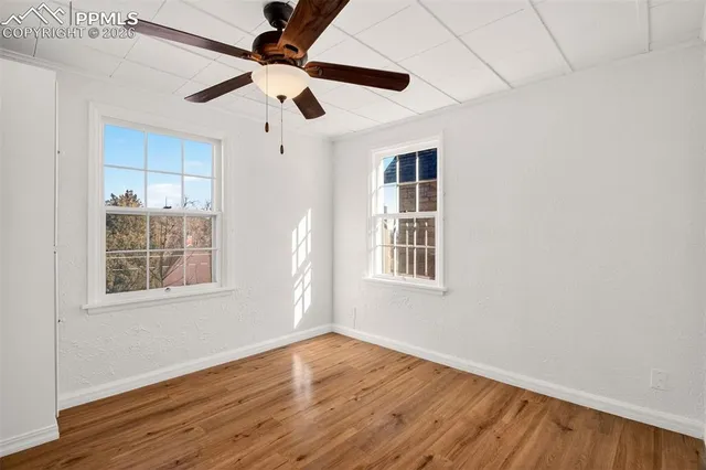 an empty room with wooden floor ceiling fan and windows