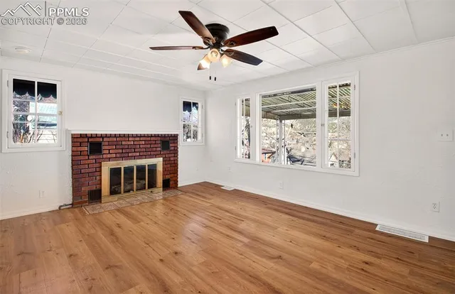 a view of an empty room with wooden floor fireplace and a window