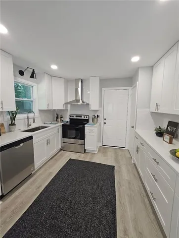 a large white kitchen with stainless steel appliances granite countertop a stove a sink a refrigerator and white cabinets with wooden floor