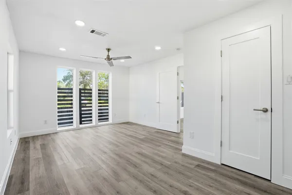 an empty room with wooden floor chandelier fan and windows
