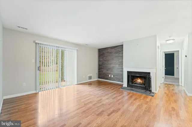 a view of an empty room with wooden floor fireplace and a window