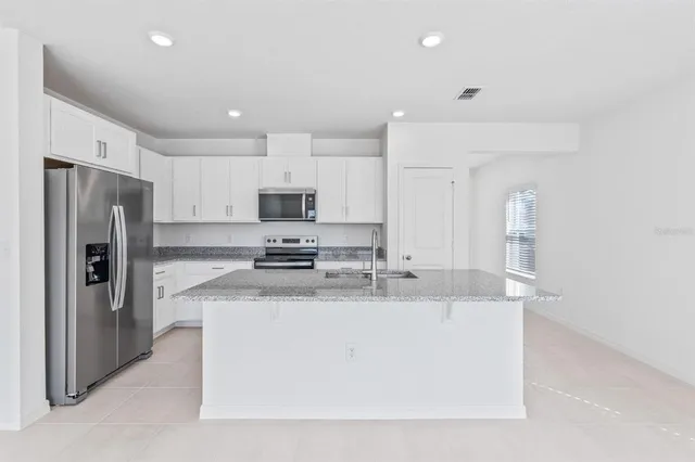 a large kitchen with stainless steel appliances granite countertop a sink a stove a refrigerator a center island and cabinets